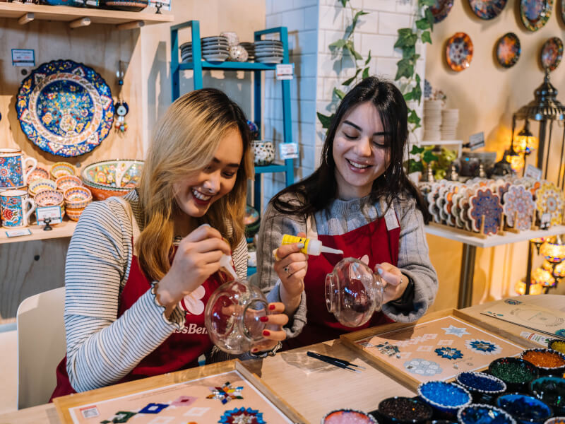Two women smiling as they make a Turkish mosaic lamp